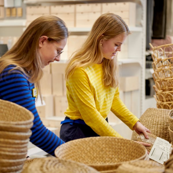 Two IKEA coworkers are putting away baskets in an IKEA store.