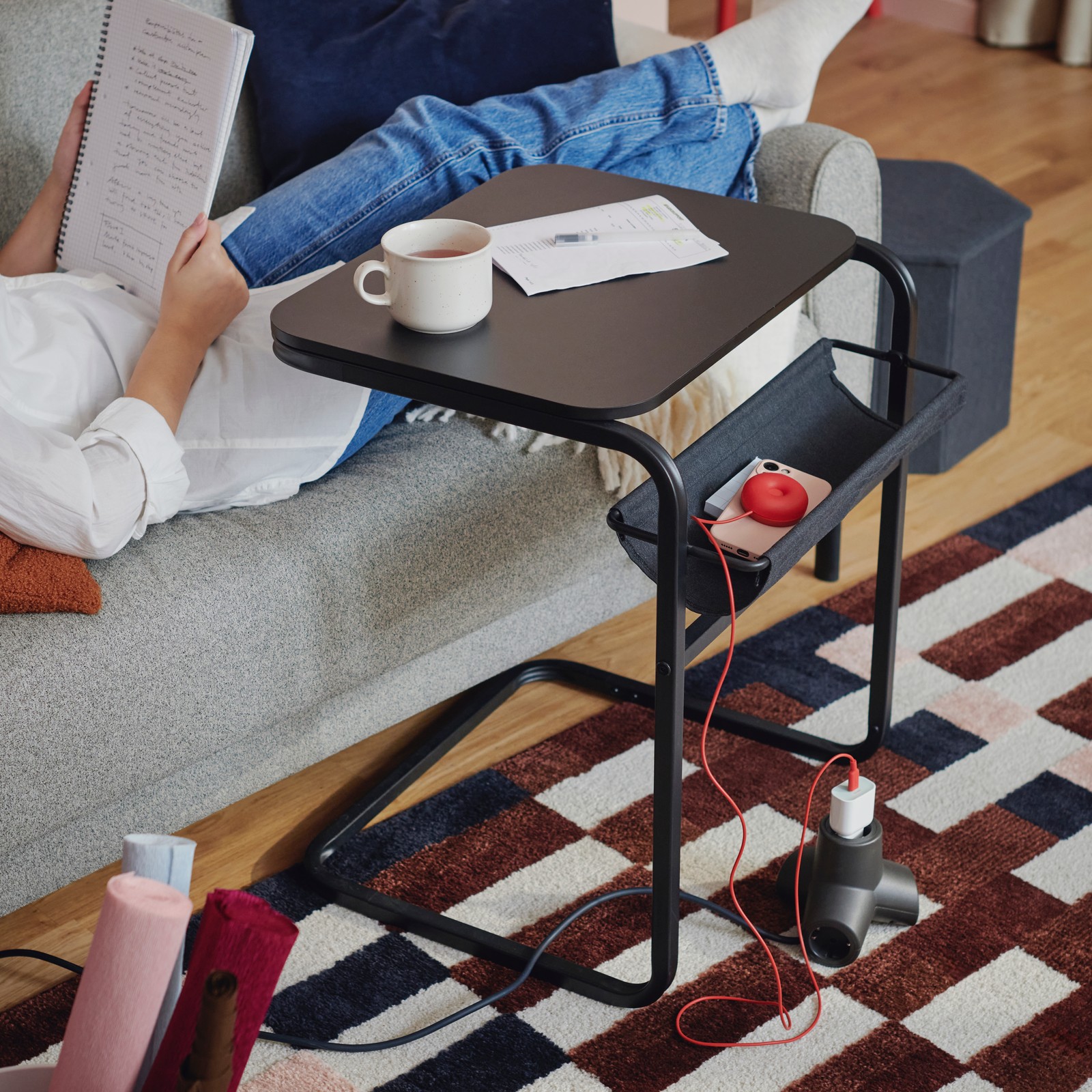 An OLSERÖD side table with a cup of coffee on top of it stands in front of a grey-beige sofa on top of a MARKBLÅMME rug.