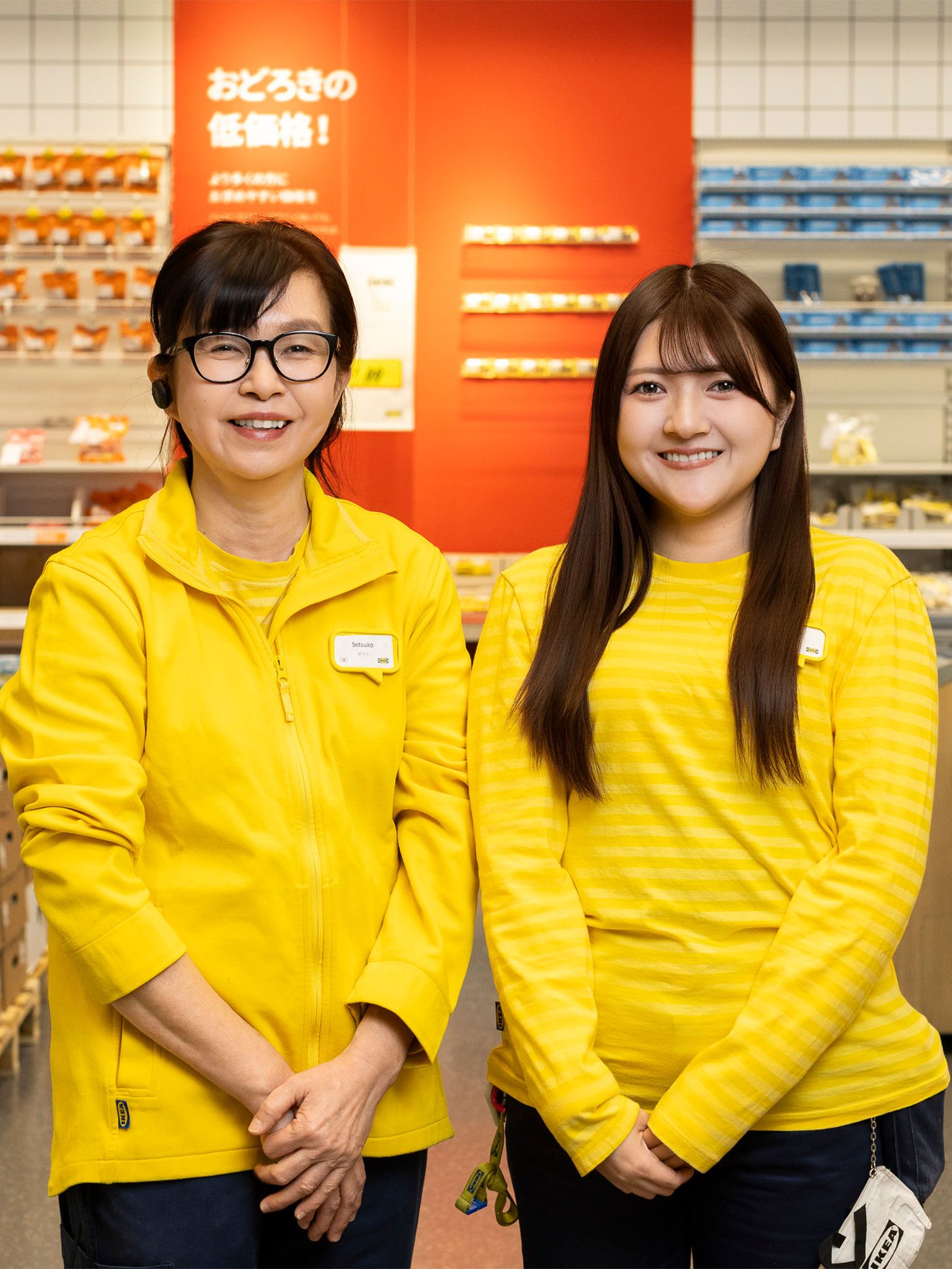 マーケットホールの棚を背景に、黄色いユニフォームを着たイケアのコワーカー2人が並んで立っている