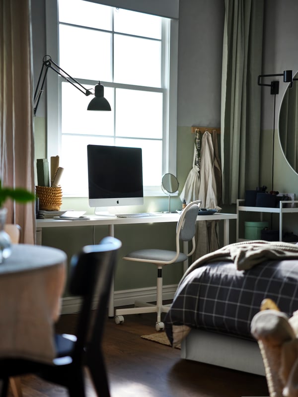 A computer on a white LAGKAPTEN/ADILS desk, a white/Vissle light grey ÖRFJÄLL children’s desk chair under a window, by a bed.