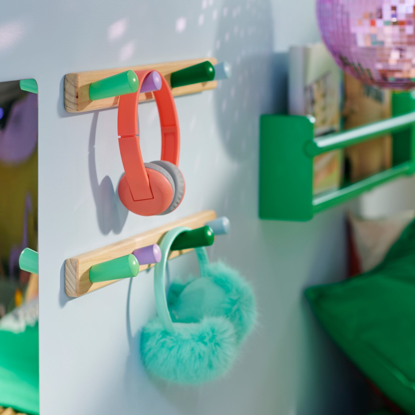 Two FLISAT racks with 4 knobs holding headphones and earmuffs on a wall beside a green FLISAT wall storage holding books.
