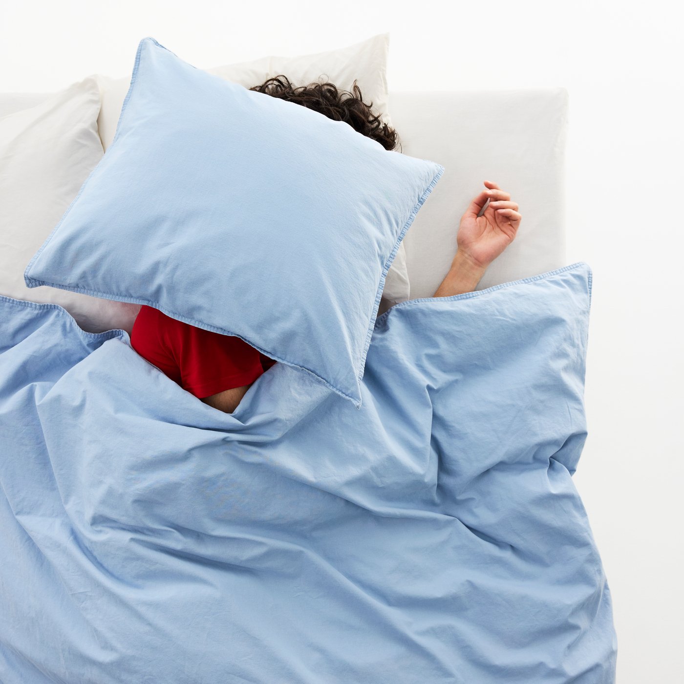 Osoba spí v posteli s polštářem na hlavě, postel je povlečená do modrého povlečení ÄNGSLILJA.
