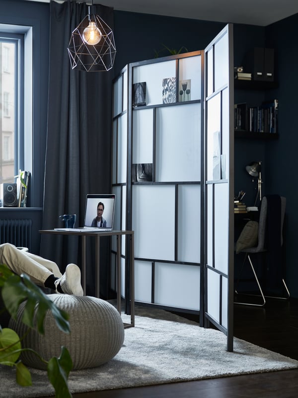 Un salon divisé en deux par un paravent RISÖR, avec un support pour ordinateur portable VITTSJÖ d’un côté, un espace de travail compact de l’autre.