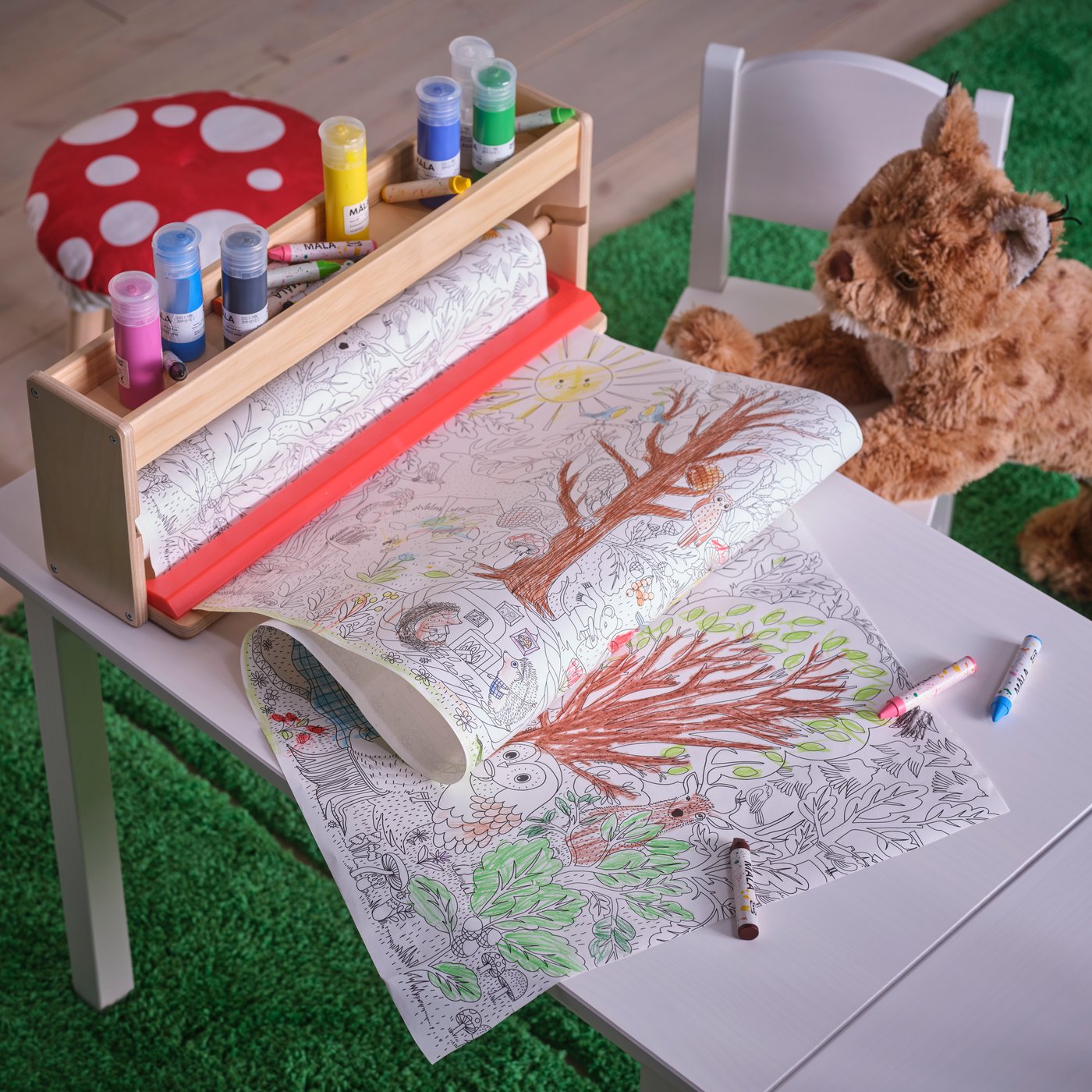 Laste meisterdamislaud, millele on lahti tõmmatud pikk SKOGSDUVA värvipaberirull. Paberil on osaliselt värvitud suur puu ja õuestseen.