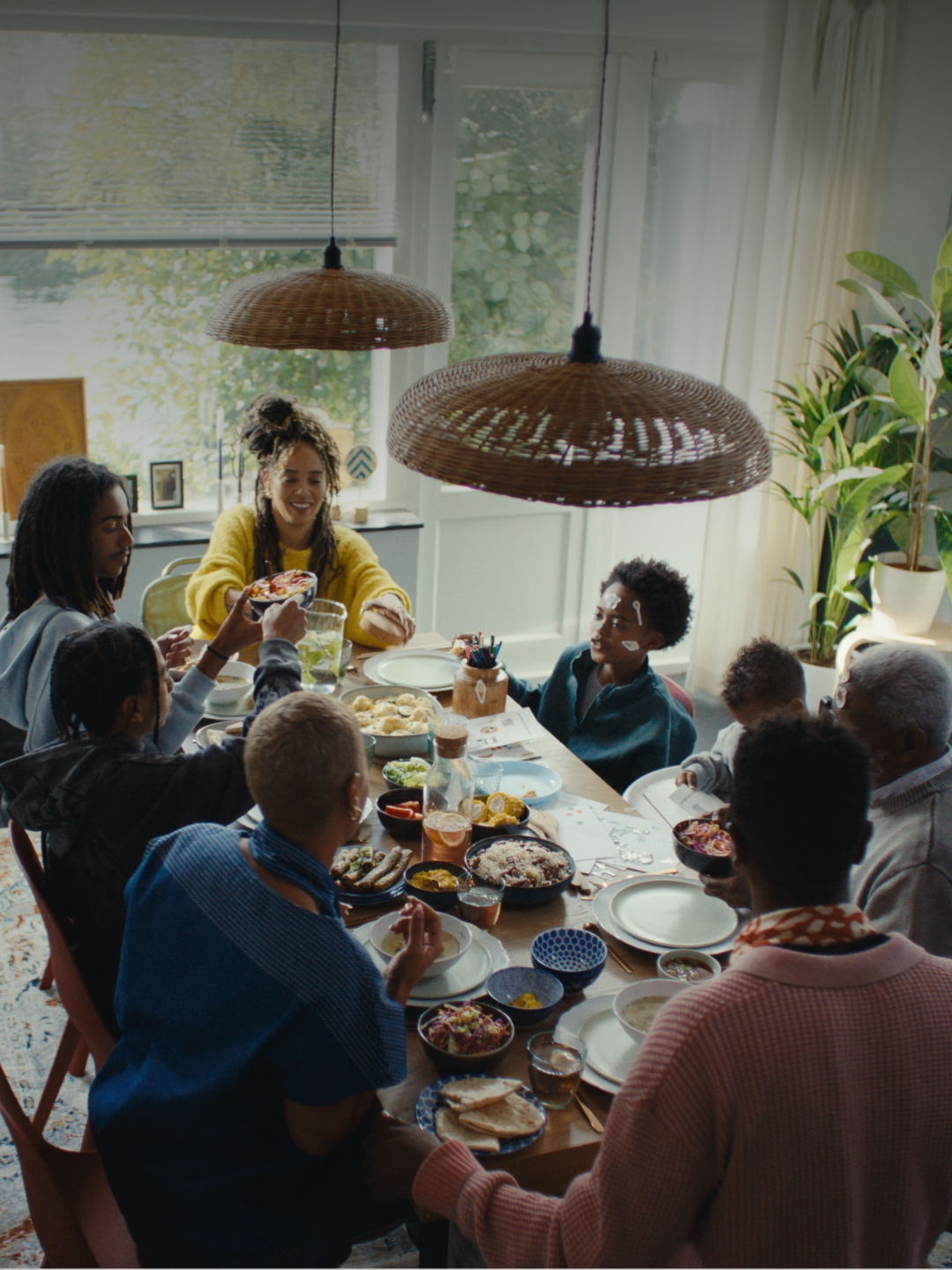 Mensen die lachend aan een tafel zitten en eten aan elkaar uitdelen.