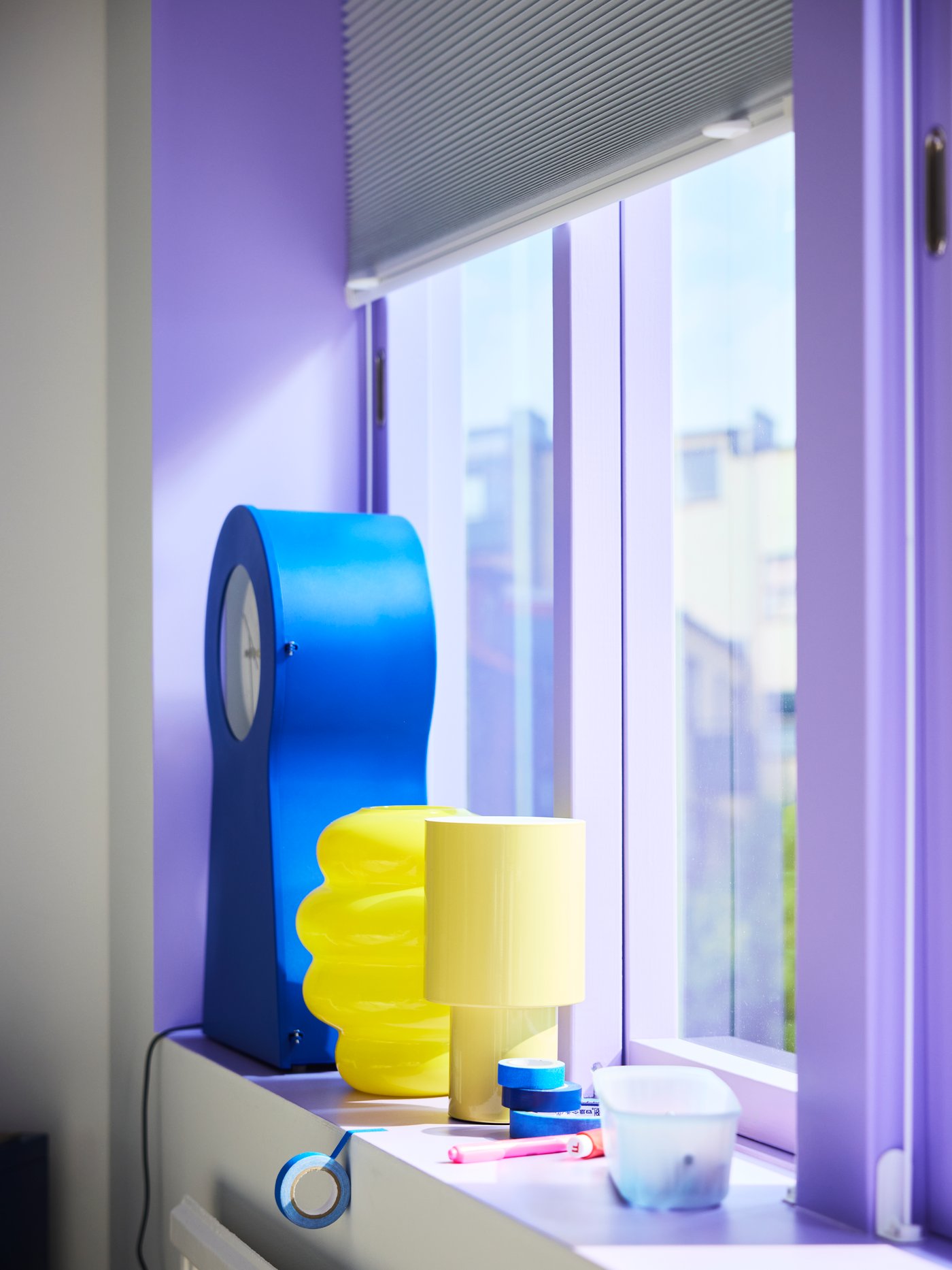 Close-up of window painted purple with bright yellow lamps and a blue IKEA PS 1995 clock standing on the windowsill.