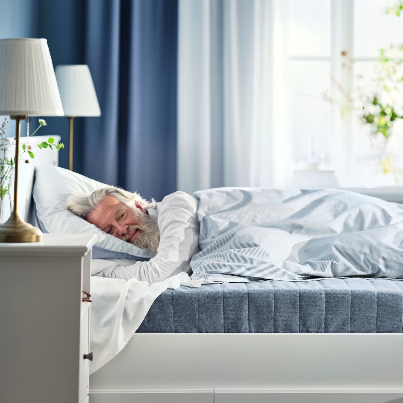A man lays on a firm/light blue VADSÖ sprung mattress.