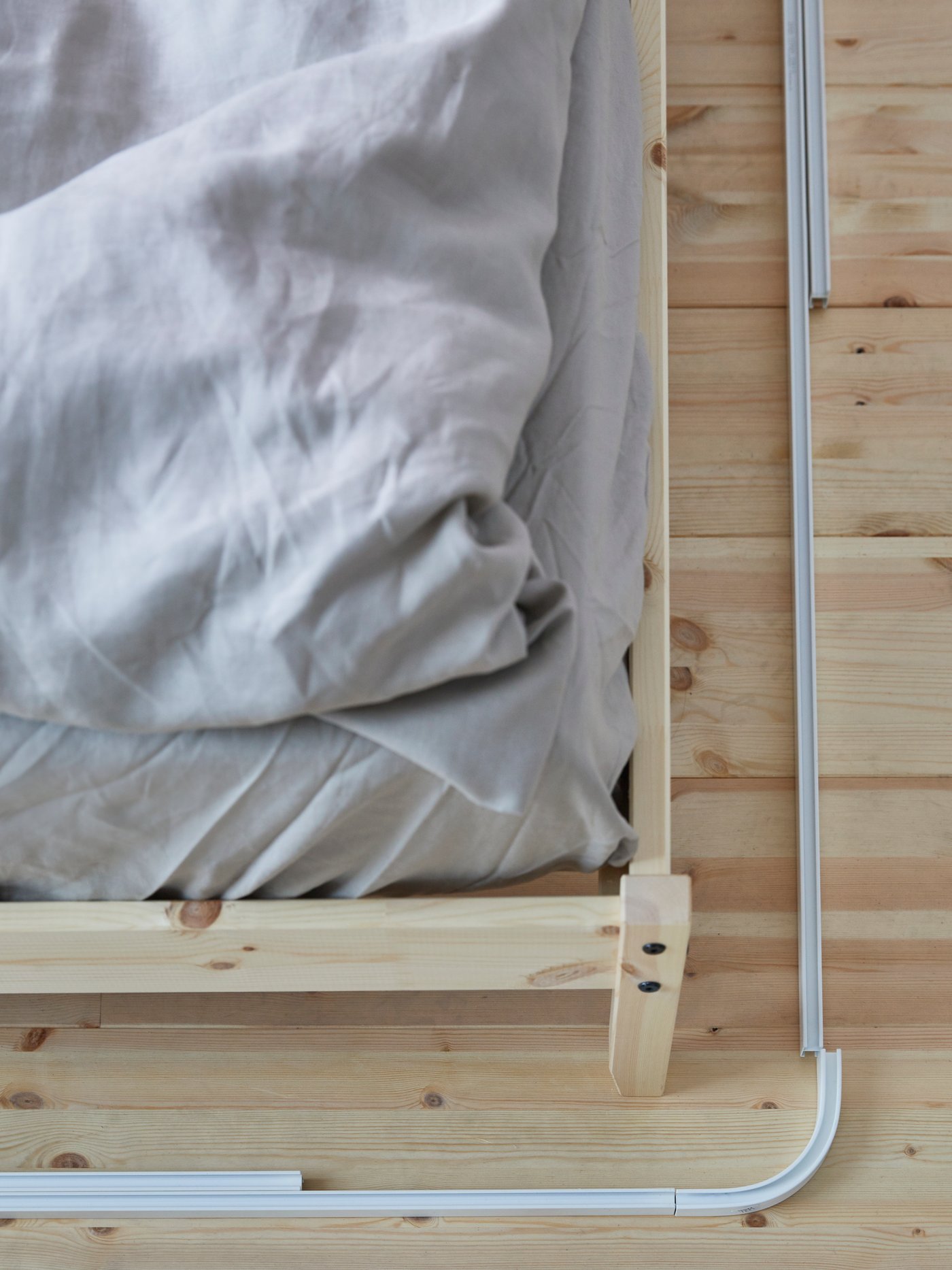 Le coin d’un lit avec des rails pour rideaux VIDGA placés sur le plancher autour du lit dans le but de les mesurer pour l’installation.