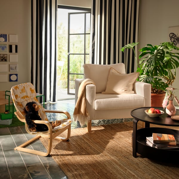 A light living room a white SALTSJÖBADEN armchair next to a small, animal-patterned POÄNG armchair holding a soft-toy chimp.