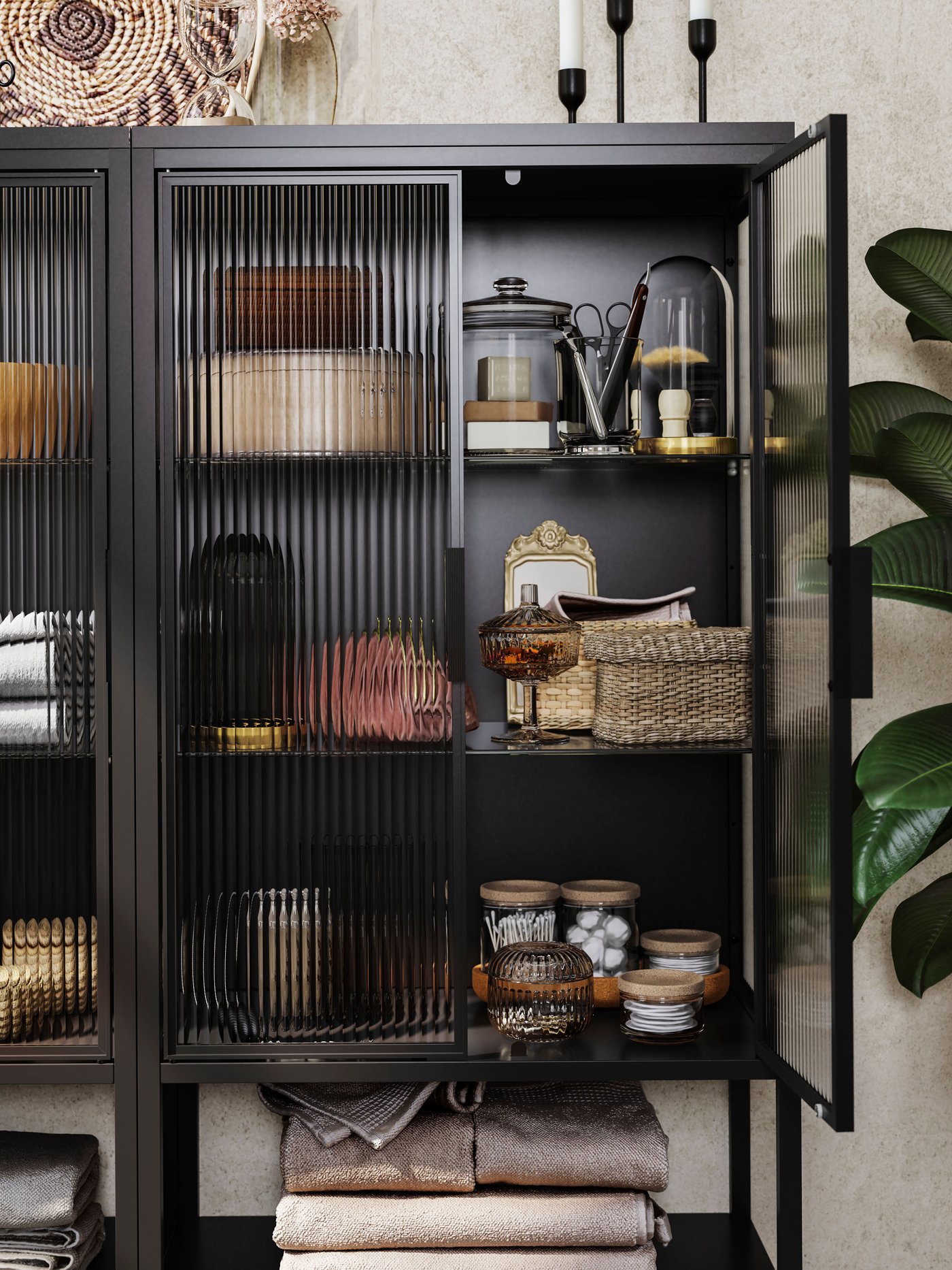 Es ist eine schwarze MOSSJÖN Vitrine mit einer geöffneten Tür zu sehen. In ihr befinden sich Dosen aus Glas, Boxen und Behälter auf Böden.