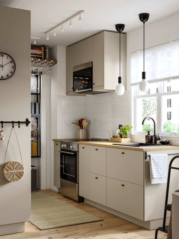 A kitchen with a window behind the sink has beige HAVSTORP kitchen fronts and a SOLNEBO over-the-range microwave.