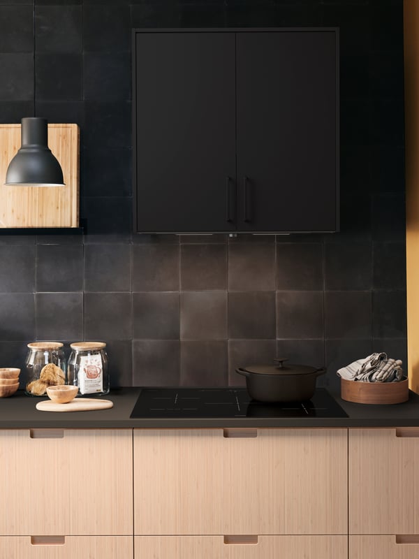 A kitchen cooking area with a MAXIMERA cabinet, a black lamp and the SÄRKLASSIG induction cooktop.