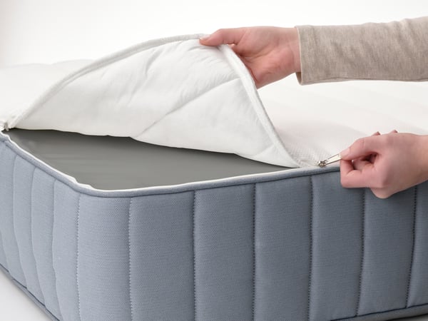 A person sitting near the corner of a medium firm/natural VATNESTRÖM pocket sprung mattress with their hand on the surface.