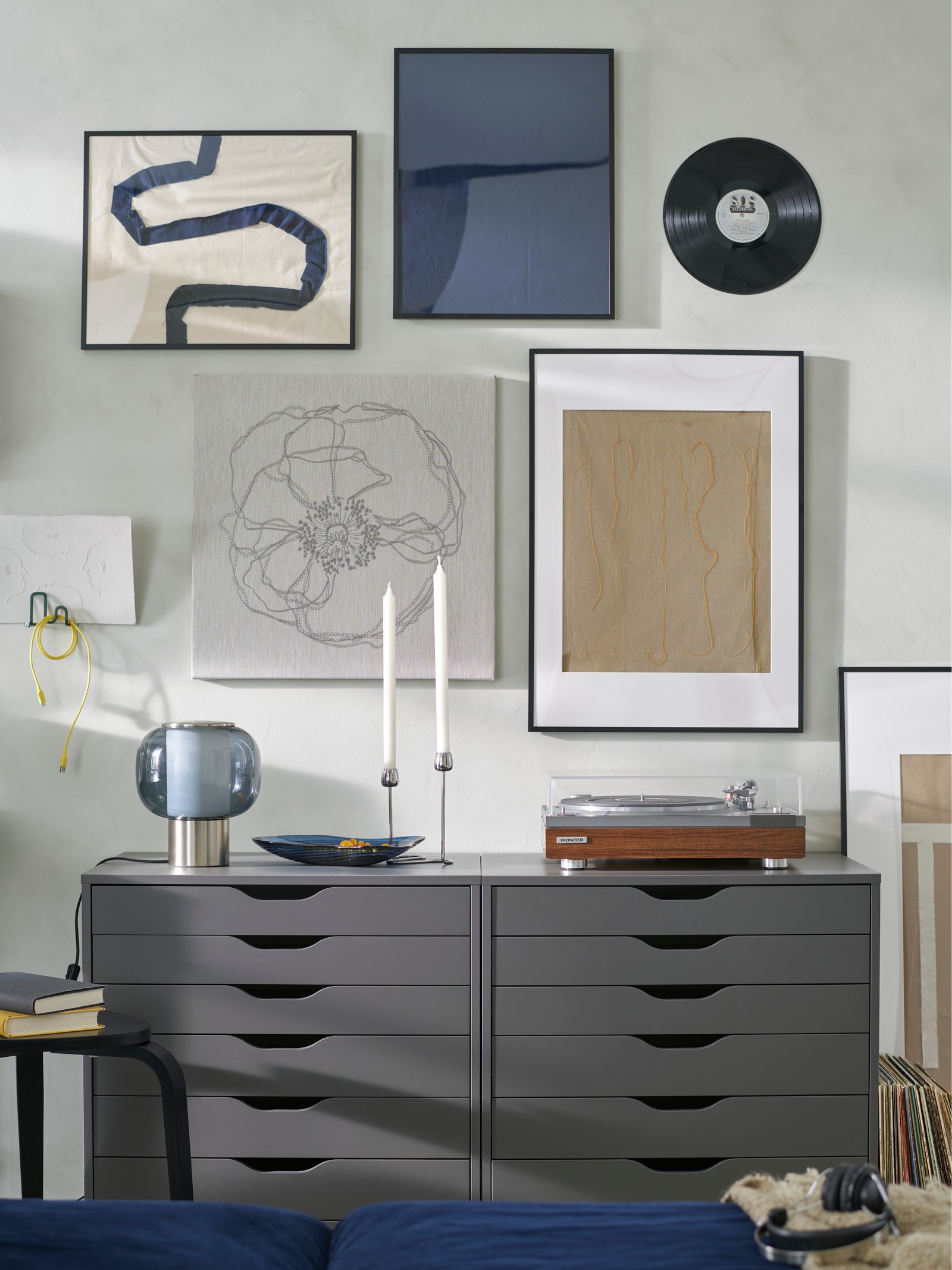 An art wall with LOMVIKEN frames and a vinyl record. A record player and HÖGVIND table lamp sit on two ALEX drawer units.