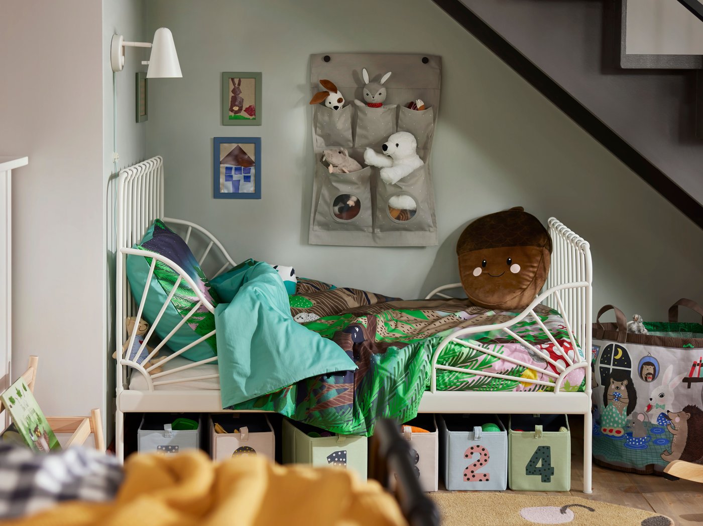 Llit infantil extensible MINNEN en un racó de l'habitació amb caixes d'emmagatzematge numerades i peluixos al damunt.