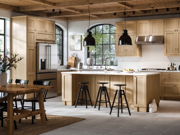 A large bright kitchen with VEDHAMN oak fronts and a kitchen island with two pendant lamps above it and bar stools in front.