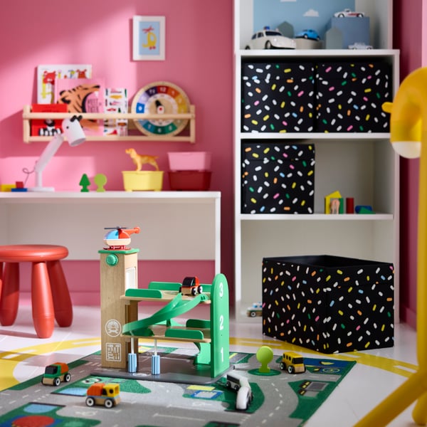 A LILLABO garage with car and helicopter placed on a play mat in a children’s room with colourful shelves and storage units.