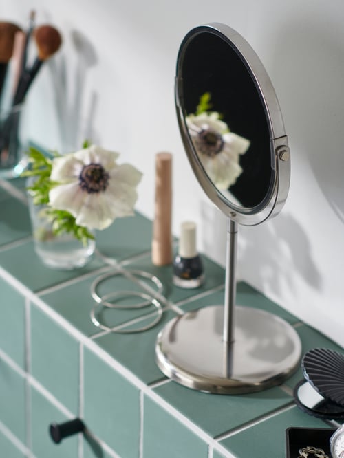 A green-tiled bathroom ledge filled with a TRENSUM mirror along with various accessories and decorations.