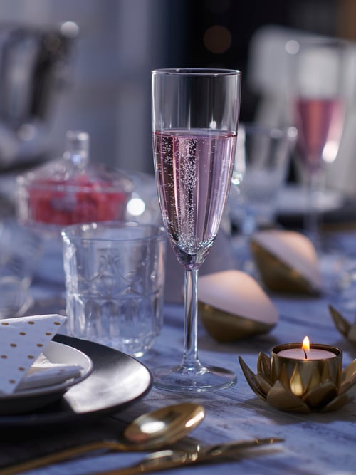 Dining room with multiple white champagne glasses with slender design, a tealight holder, a grey side plate and a glass.
