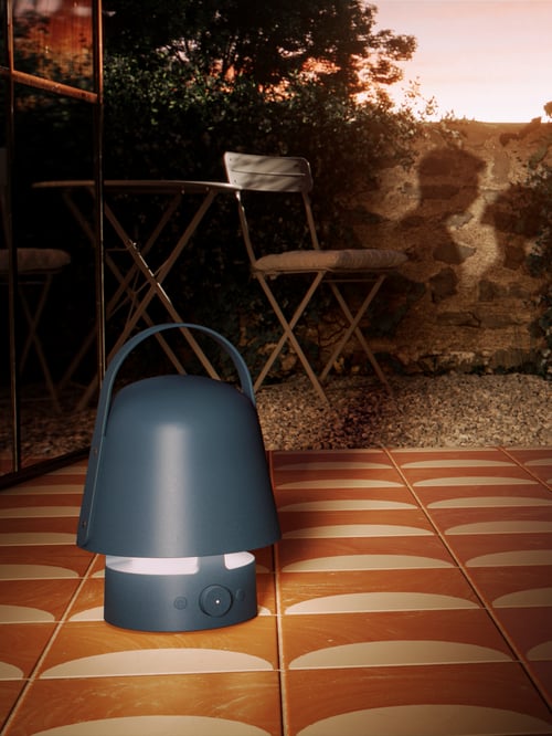 The VAPPEBY Bluetooth speaker lamp is in a tiled doorway to a walled garden; a shadow of a couple is on the outdoor wall.