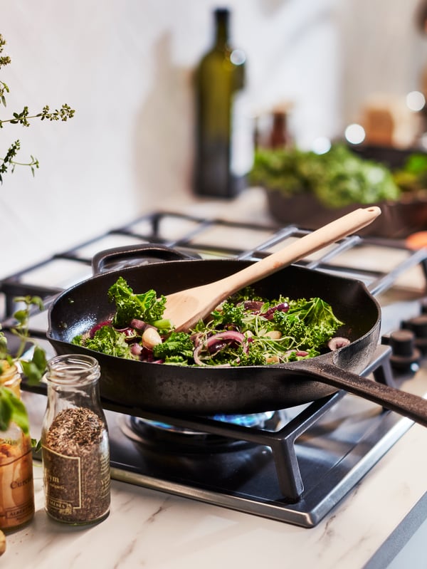 Vegetables are being fried in a VARDAGEN black frying pan made from cast iron. A wooden spatula is resting on the pan.