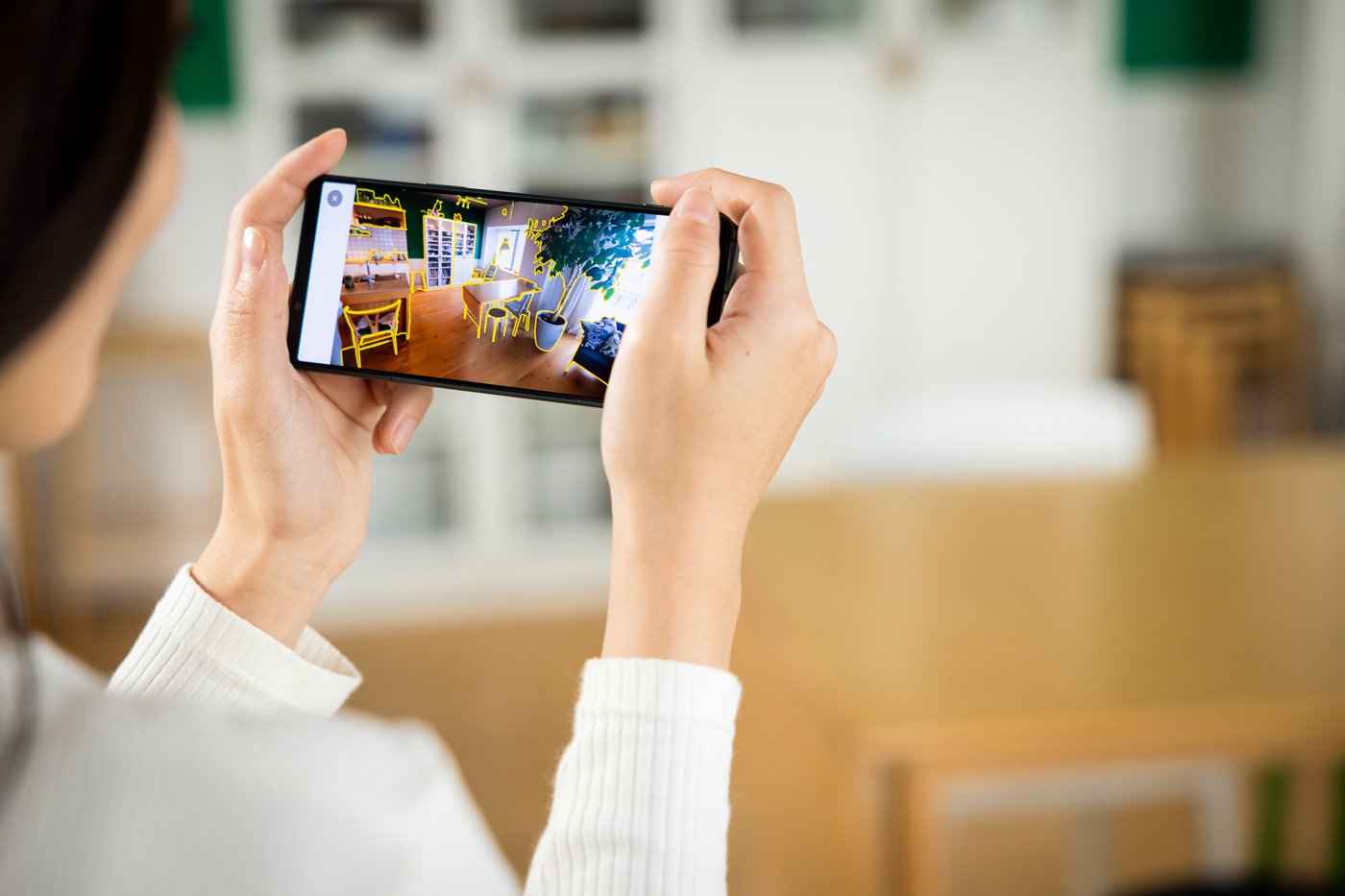 A person is designing a room using a planner on their smartphone, which they are holding horizontally. 
