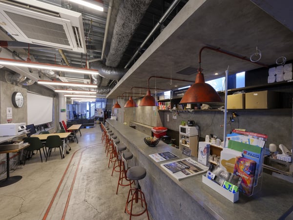 赤いペンダントライトが印象的なカウンターとテーブル席が並ぶ、自然光が差し込むモダンな空間