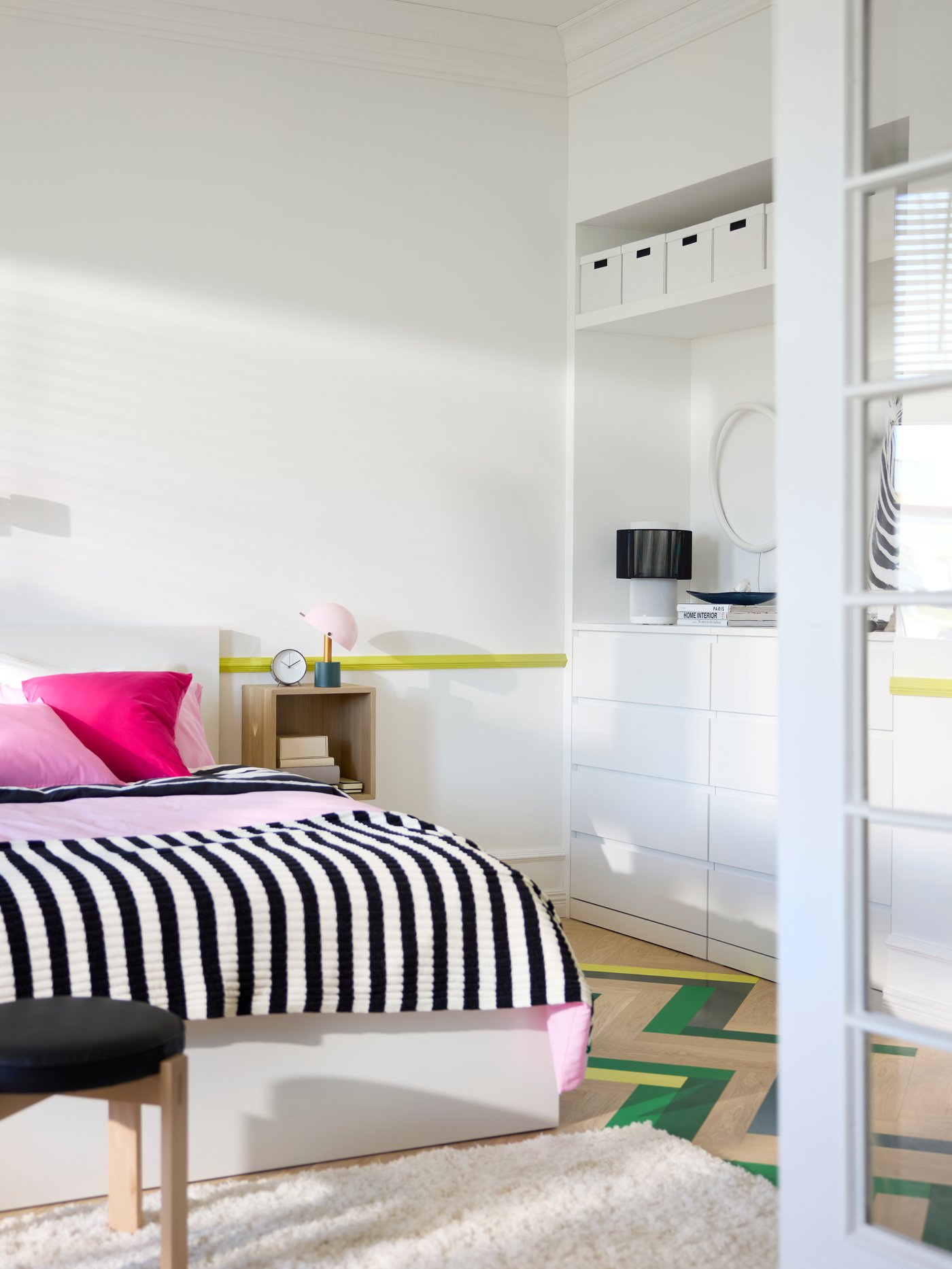 Utsikt över sovrum genom öppna glasdörrar, med krispigt vita väggar, förvaringslösningar och en dubbelsäng i mitten.