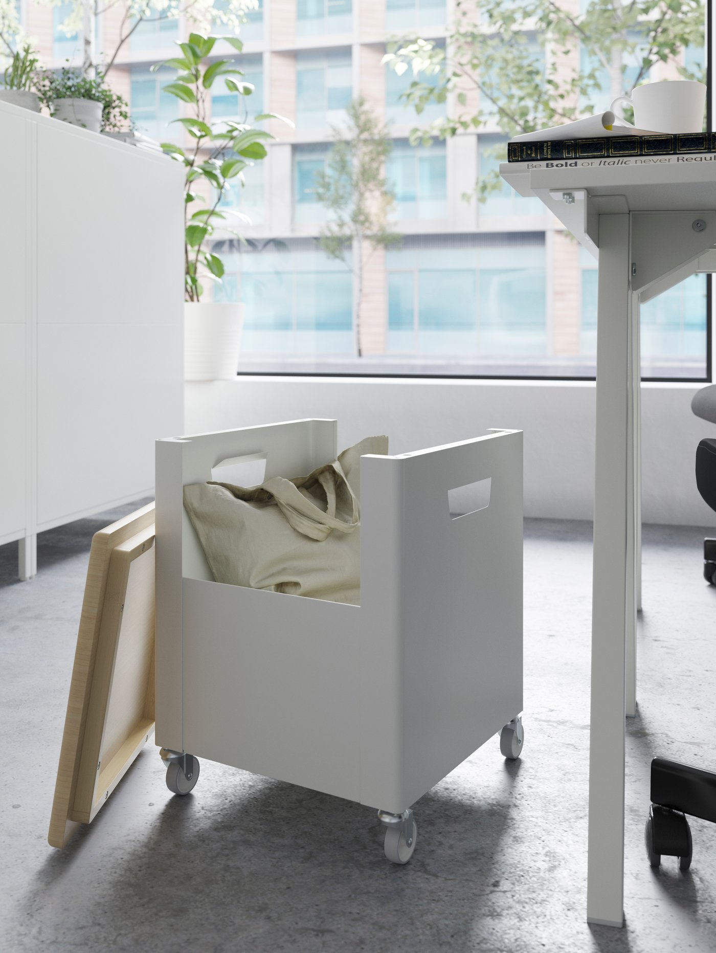 A white storage unit on castors with the bamboo lid off and a beige totebag in it, beside a desk.