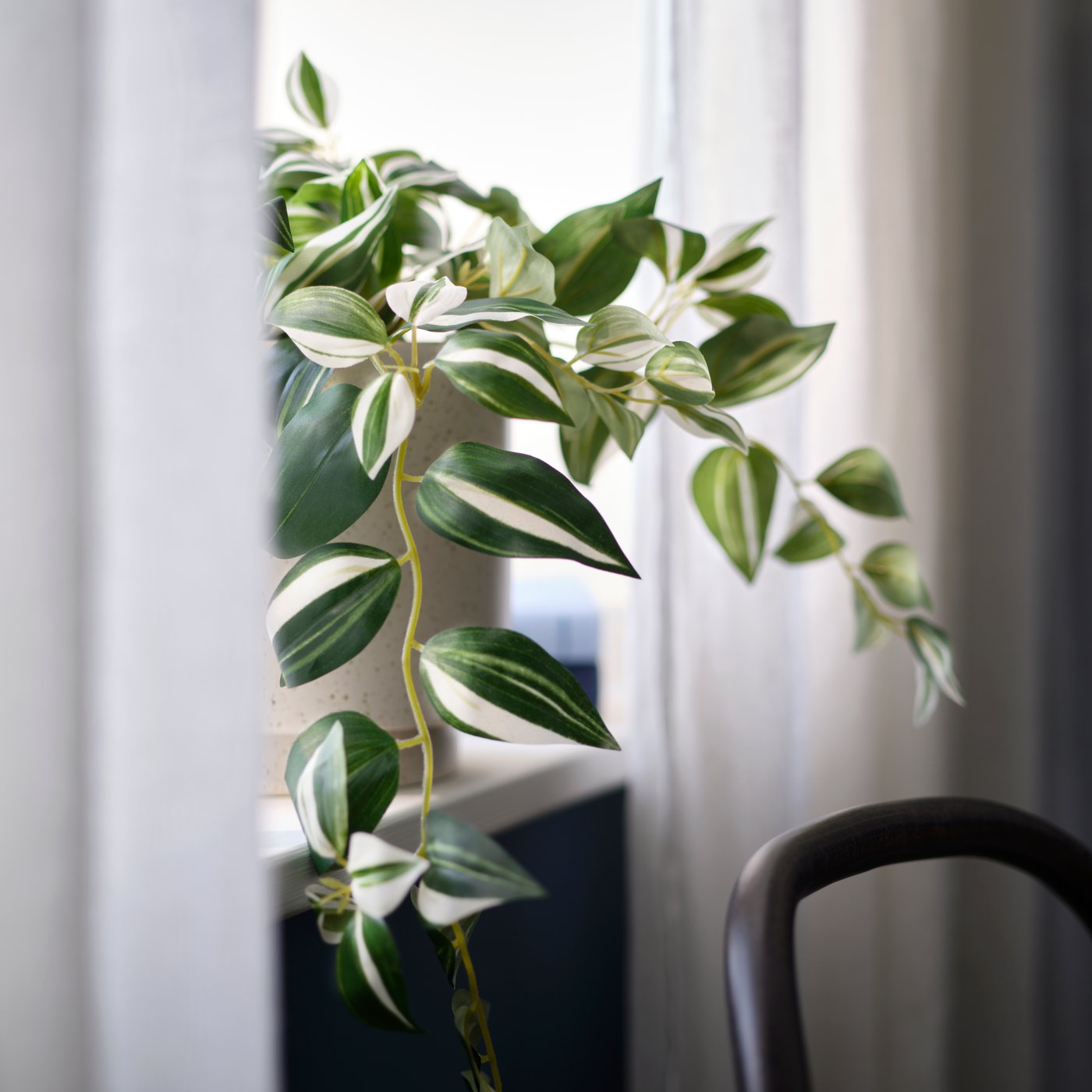 A FEJKA artificial potted plant in a pot placed on a windowsill with sheer curtains.