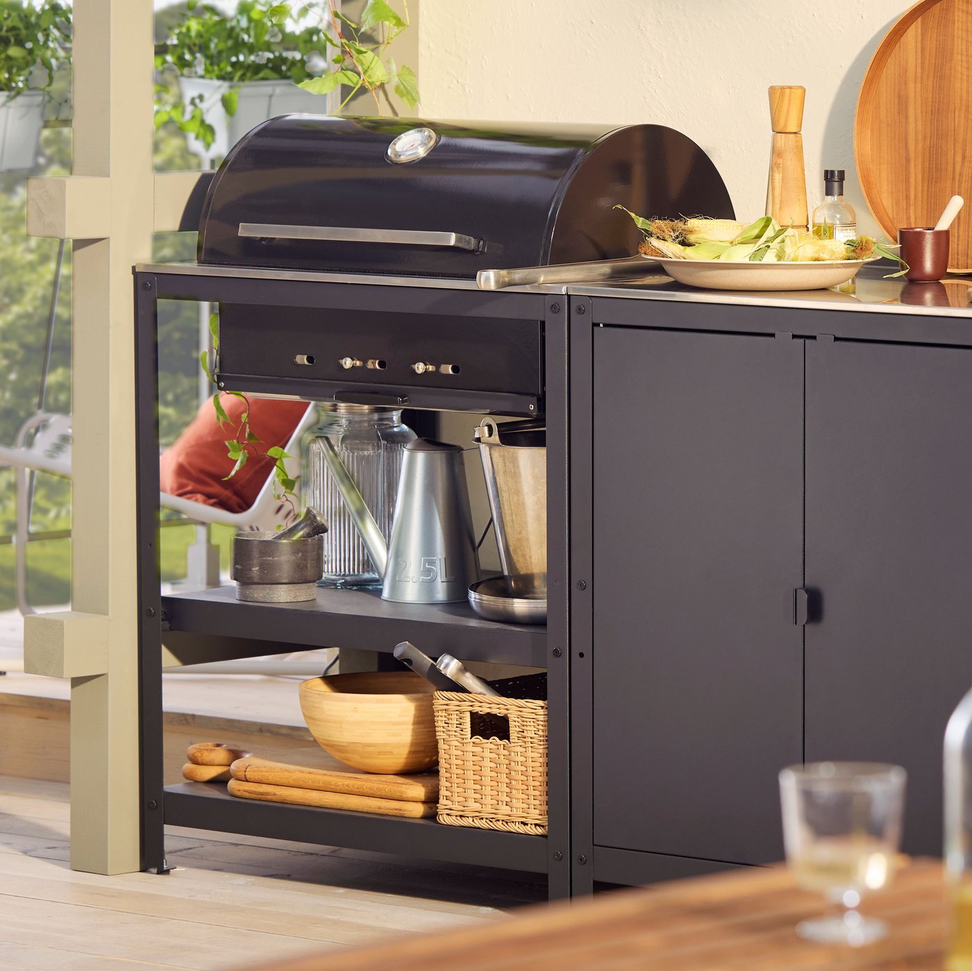 Un porxo al capvespre amb una barbacoa amb illa de cuina exterior GRILLSKÄR d'acer inoxidable de color negre amb accessoris de cuina.