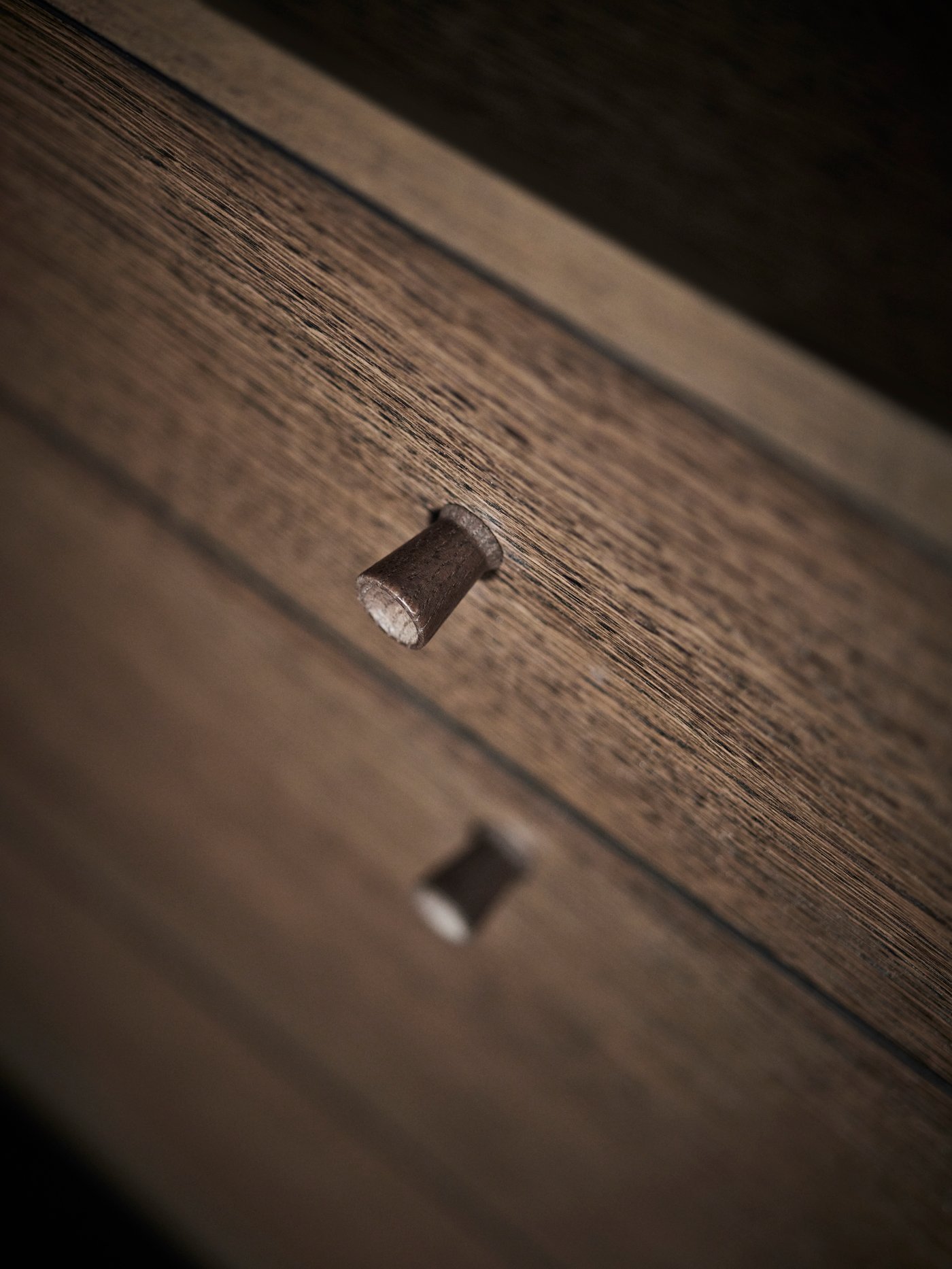 Gros plan de l’avant d’une commode 6 tiroirs TONSTAD plaqué chêne brun, avec deux des boutons en chêne massif.