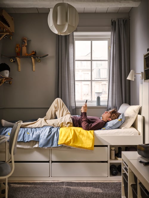 Modernes Teenagerzimmer mit einem SLÄKT Bettgestell mit Schubladen + Federholzrahmen, einer FUBBLA LED-Wandleuchte, einem TRUBBNATE Hängeleuchtenschirm und VÄNKRETS Bettwäsche in Blau und Gelb.
