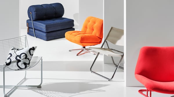 Five different chairs from the Nytillverkad collection are placed in a white room. Among them is a blue VÅRKUMLA chair bed.