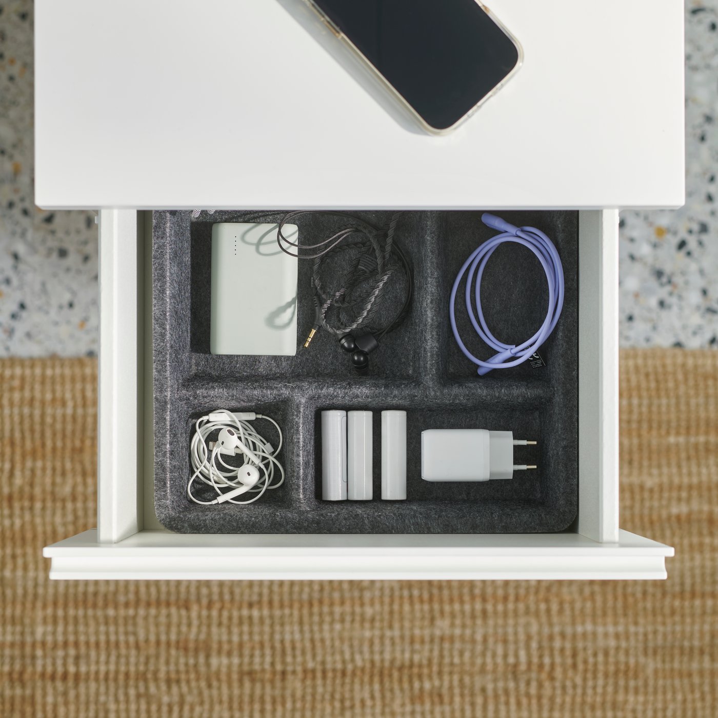 Vista cenital de una cómoda STORKLINTA blanca con el cajón superior abierto, que contiene cables y dispositivos electrónicos organizados.