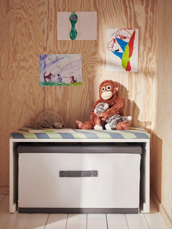 Bílá lavice SMÅSTAD, pod kterou je zasunutá bílo-šedá krabice JÄTTEBJÖRN s víkem. Na lavici sedí plyšový orangutan DJUNGELSKOG.