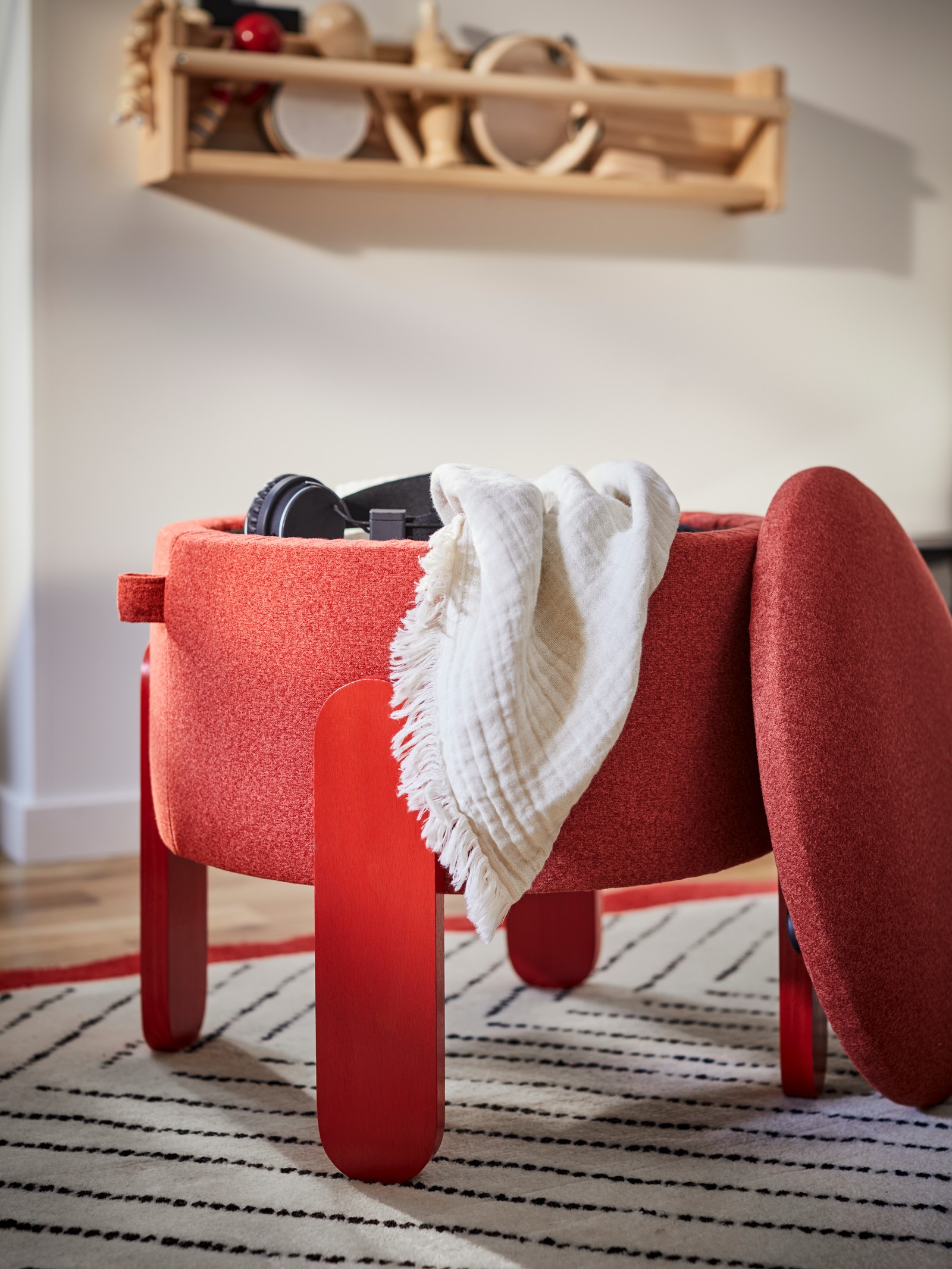 A FÖRLUNDA pouffe with storage with its seat off stands on an UNDERVISNING rug near a FLISAT wall storage on the wall.