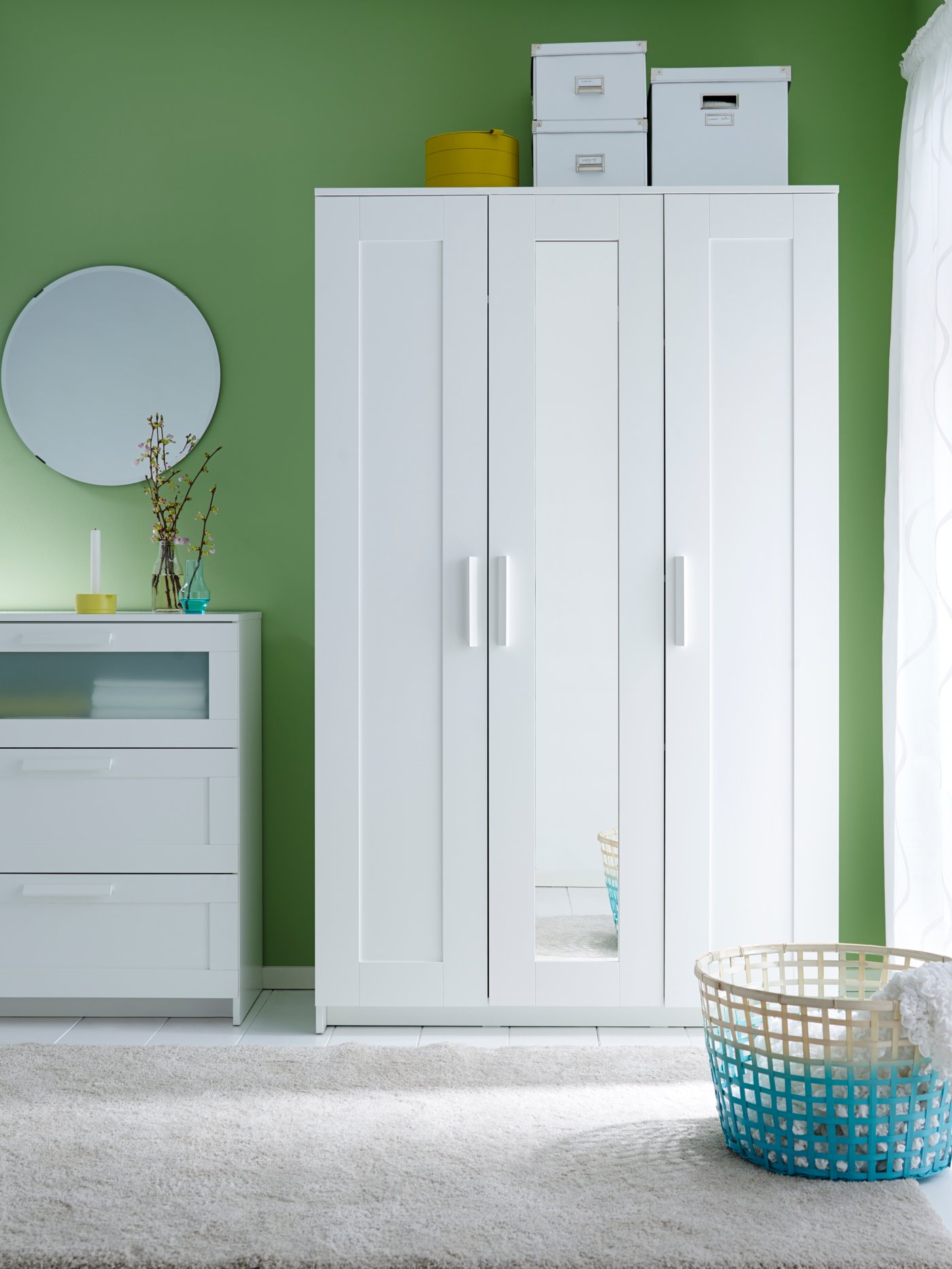 Armari BRIMNES de tres portes blanc amb una porta amb mirall al mig i caixes TJENA blanques a sobre i una calaixera BRIMNES blanca al costat.