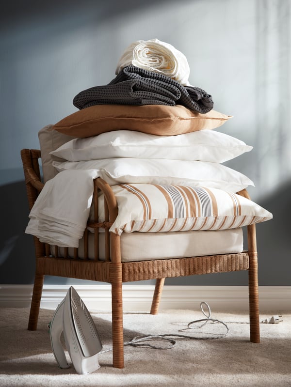 Literie dans du linge de lit ÄNGSLILJA blanc, couvre-lit gris foncé et coussin beige foncé empilés sur un fauteuil HOLMSTA/FRÖKNABO.
