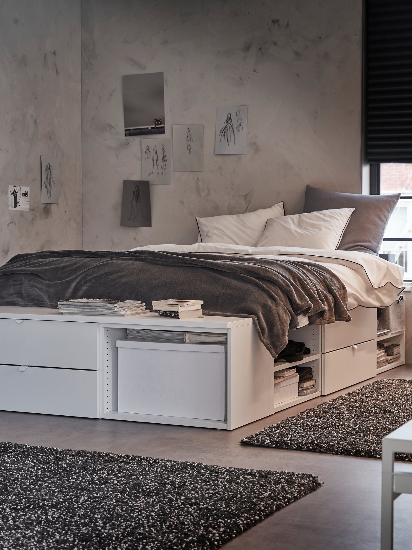 Ložnice s postelí PLATSA se zásuvkami, policemi a lavicí stojí u okna s tmavě šedými žaluziemi.