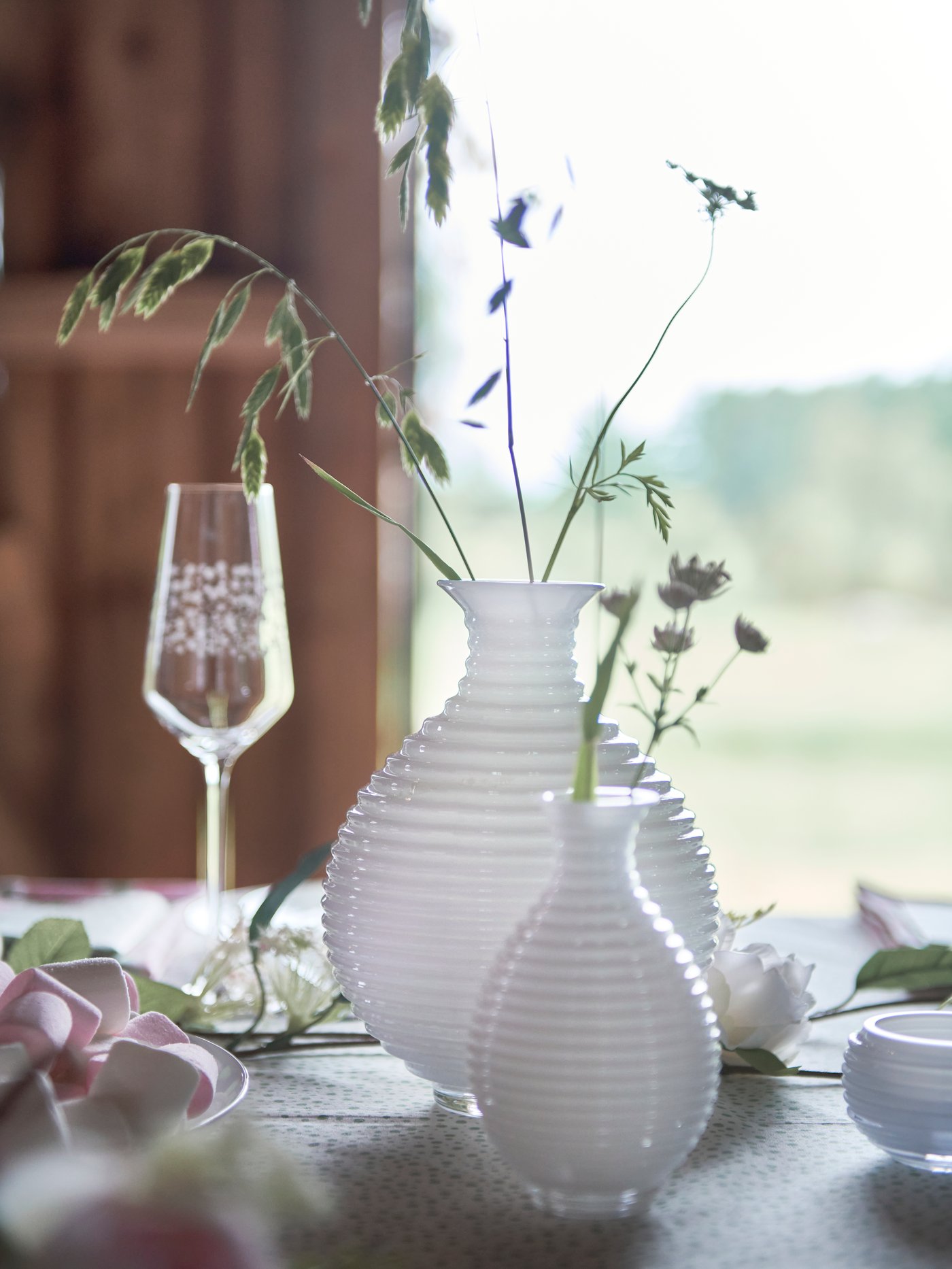 Two INBJUDEN vases in different sizes and containing springs of flowers act as centrepieces on a table at a party.