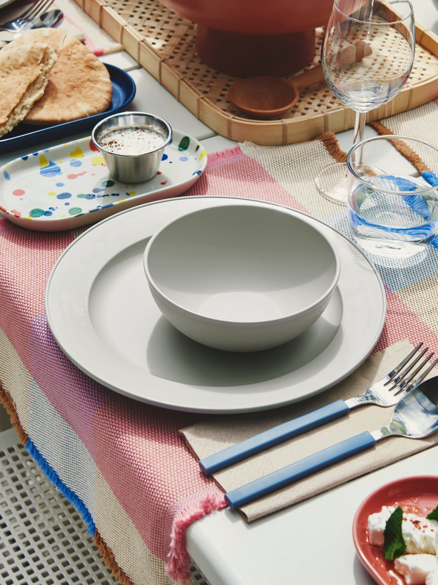 An outdoor dining table is set with a green-grey SIMKRABBA plate, with various dishes and glasses arranged around.