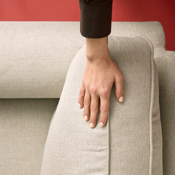 A hand gently placed on a cushion of a three-seat EKTORP Kilanda light beige sofa.