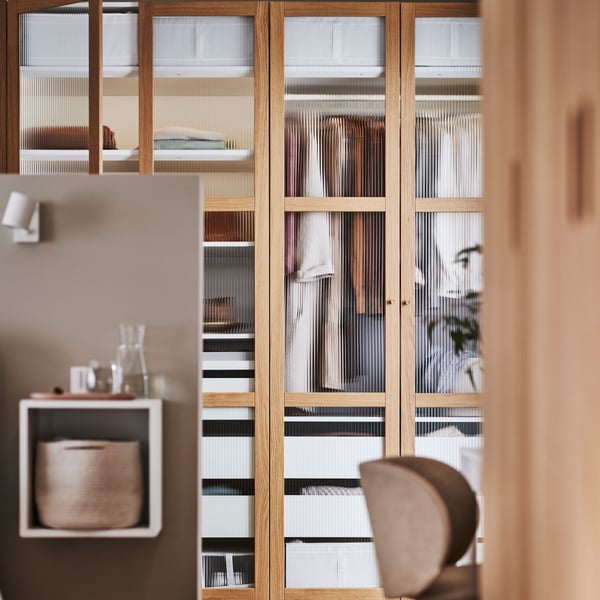 Un clóset PAX con puertas de madera y vidrio que permiten ver las prendas en el interior.