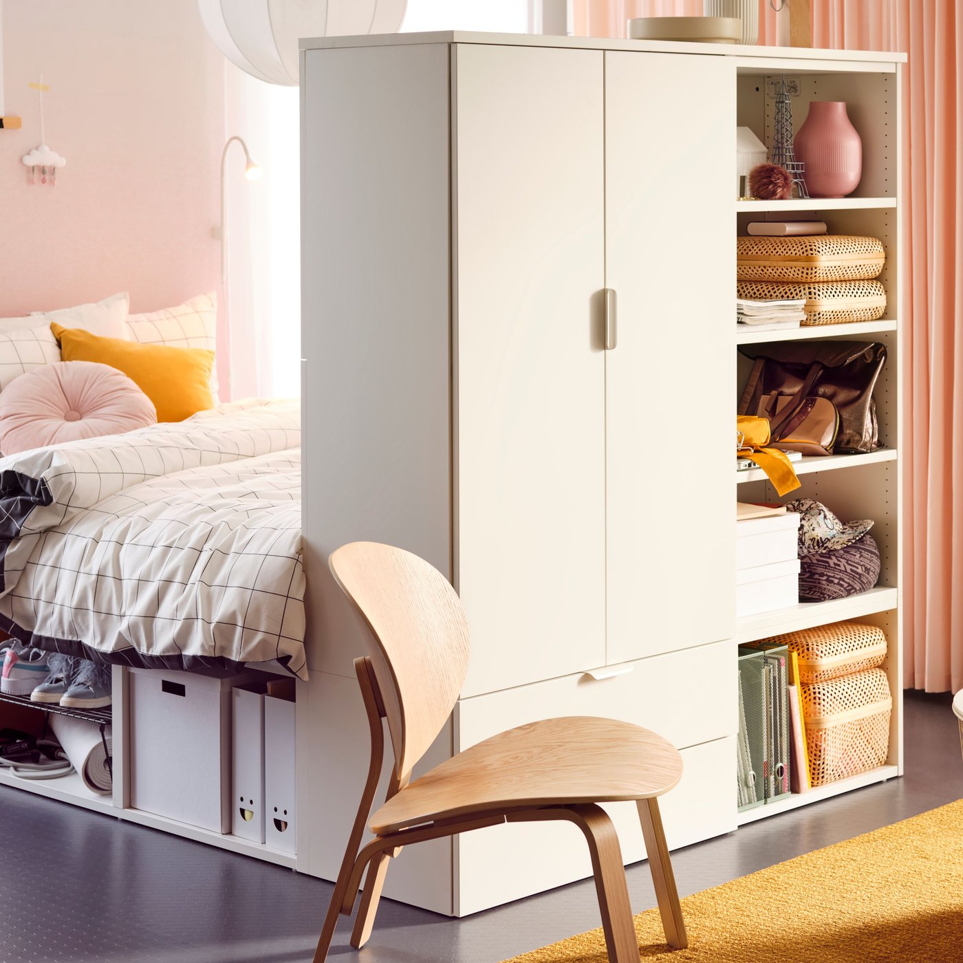 Camera da letto con struttura letto PLATSA con oggetti e cesti sui ripiani e un tappeto giallo sul pavimento. La camera è divisa in 2 tramite un guardaroba e uno scaffale .