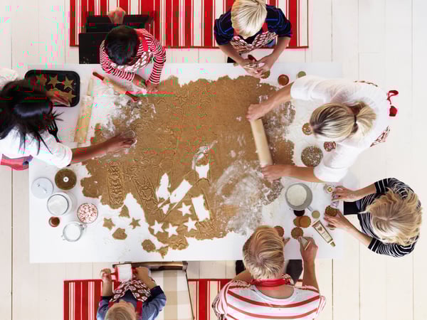 Un gruppo di bambini e adulti lavorano un grande pan di zenzero steso su un tavolo da pranzo.
