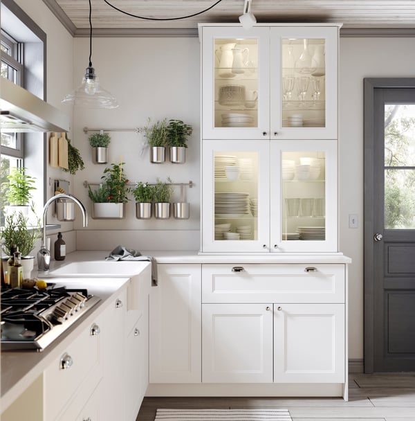 A white SEKTION kitchen. White tall cabinet with glass inserts along wall. Silver KUNGSFORS rails along wall
