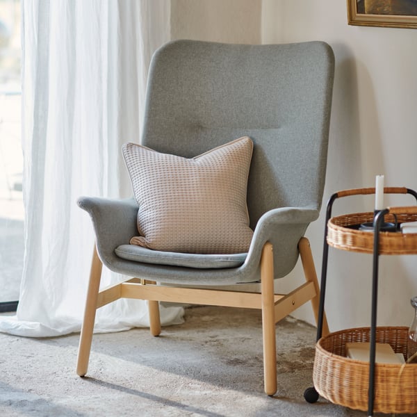 A VEDBO armchair in Gunnared light green is in a corner of a room with concrete floors next to a white DYTÅG curtain.