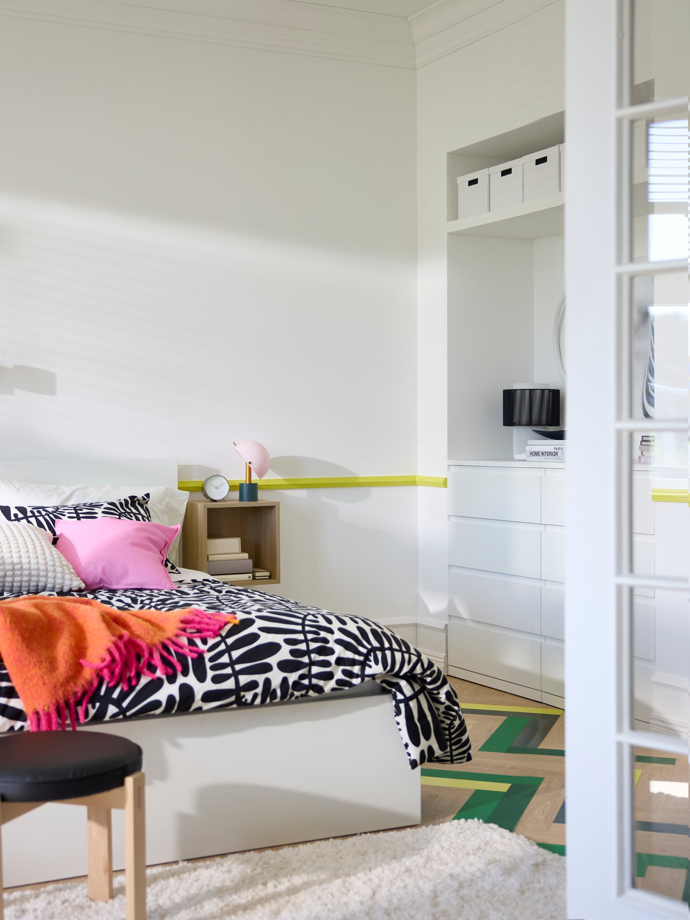 View of bedroom through open glass doors, with crisp white walls and storage combinations, double bed in middle.