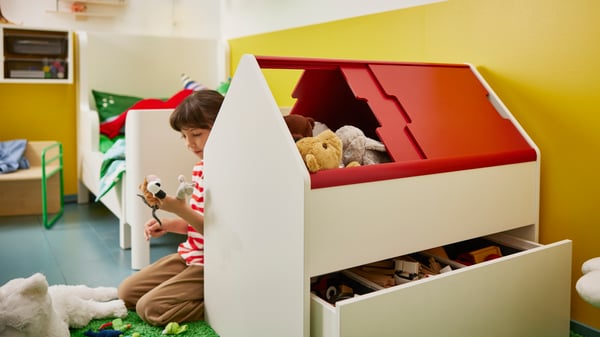 Girl playing with soft toys, sitting behind VITBJÖRN storage unit with drawer full of toys. BUSUNGE extendable bed in back.